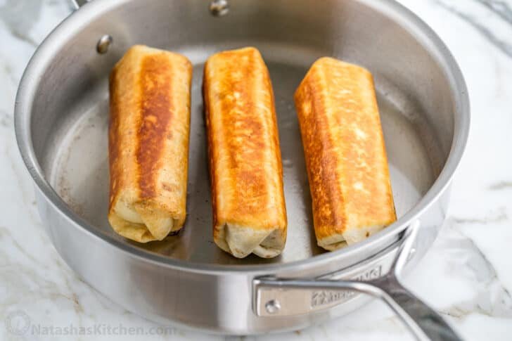 These Breakfast Burritos will make a breakfast person out of you. Crisp on the outside and filled with egg, ham, and cheese. Easy freezer breakfast burritos! 3 golden brown breakfast burritos sautéed in a pan for a crunchy bite