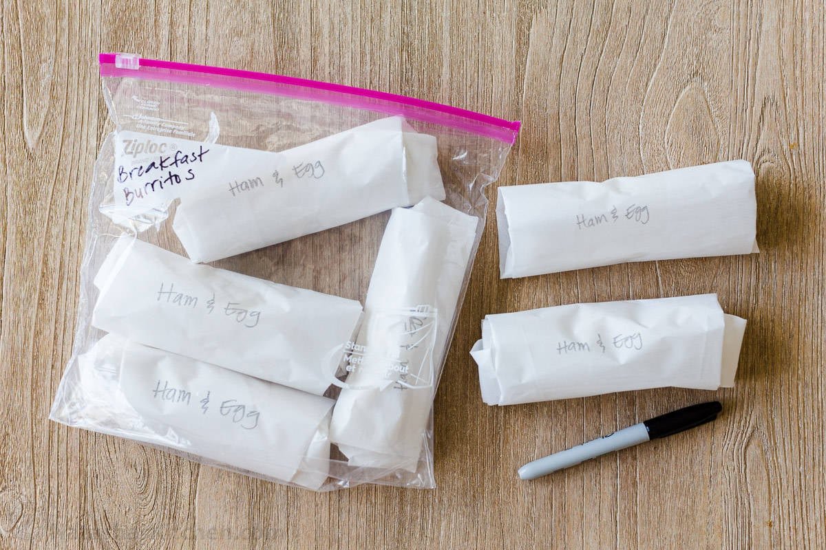 These freezer-friendly Breakfast Burritos will make a breakfast person out of you. Crisp on the outside and filled with egg, ham, and cheese. Easy freezer breakfast burritos! Breakfast burritos wrapped in parchment paper, labeled, and stored in a freezer bag for freezer storage