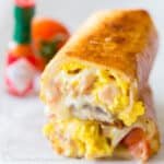 Stacked Breakfast Burritos sliced in half to showcase egg, ham, and cheese.