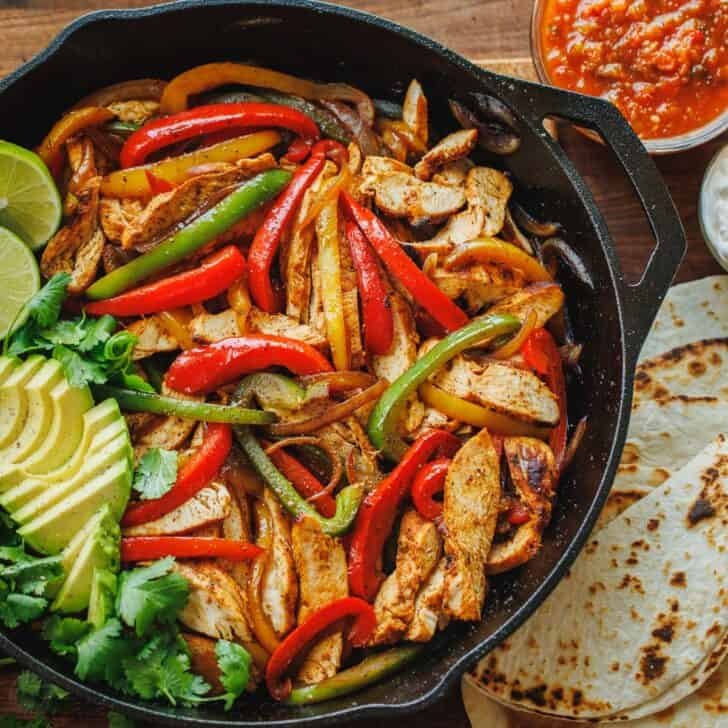 Chicken fajitas served out of a skillet with tortillas and sauces