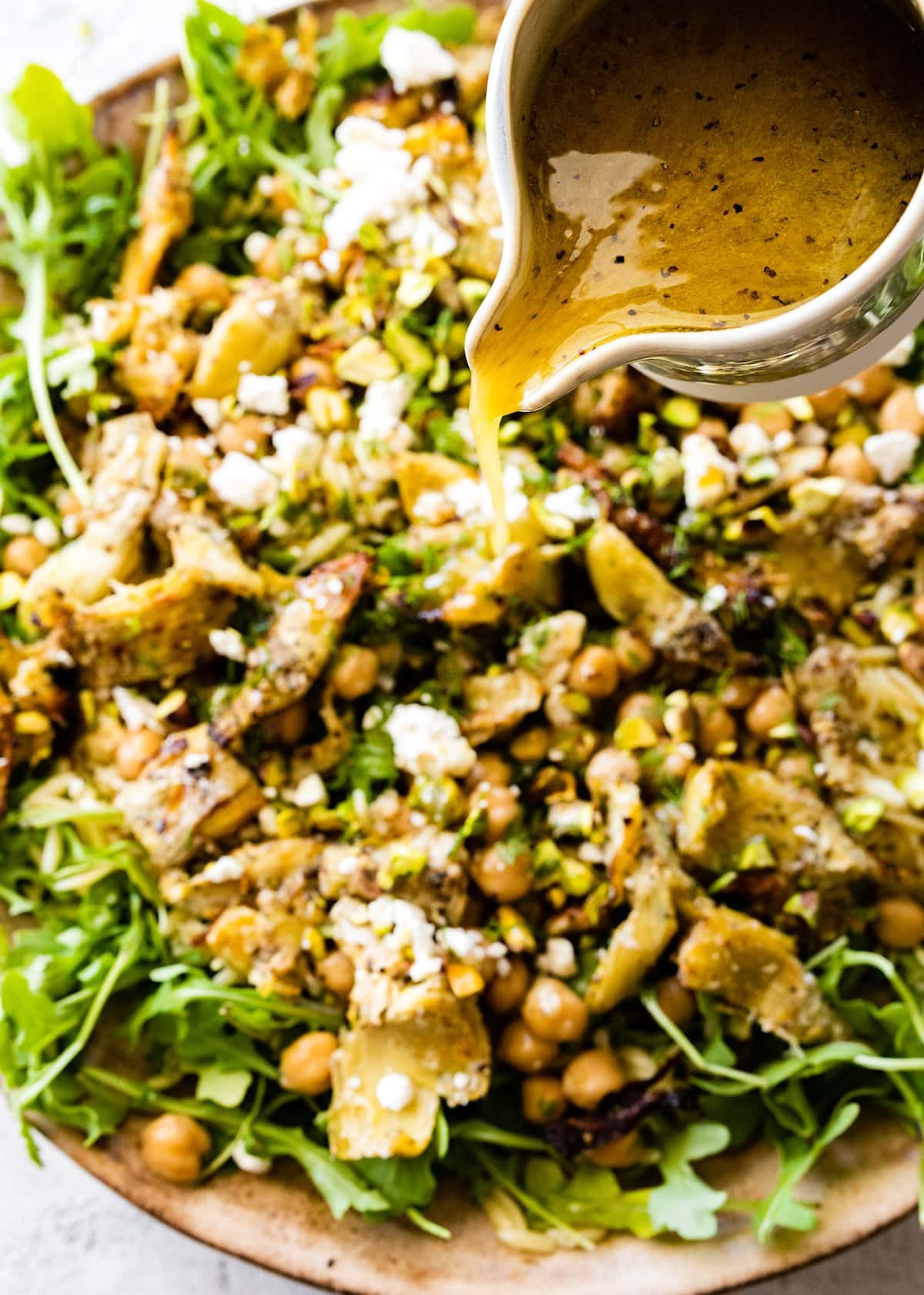 lemon vinaigrette being poured over roasted artichoke chickpea orzo salad. 