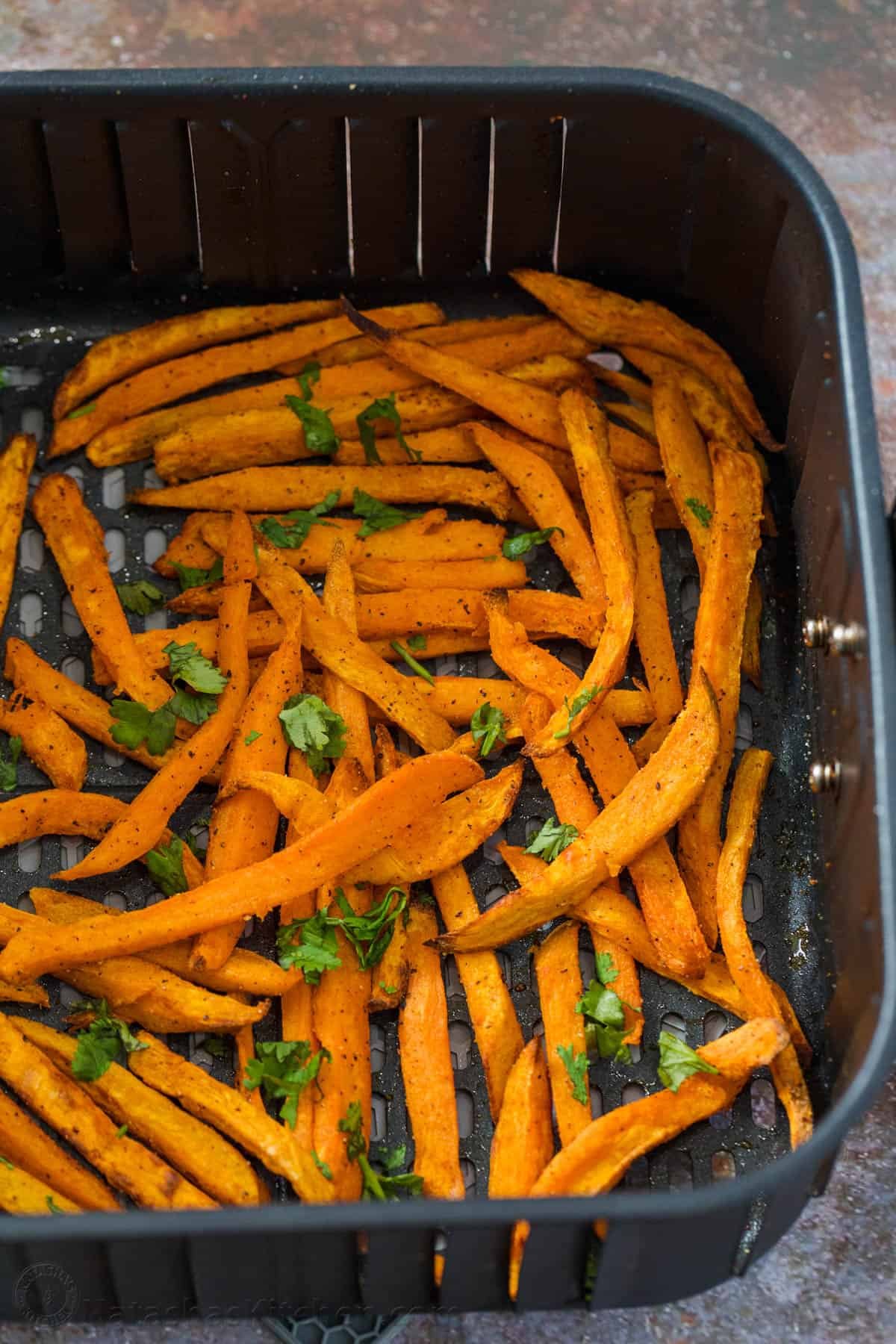 Sweet potatoes in an air fryer basket tossed with greens.