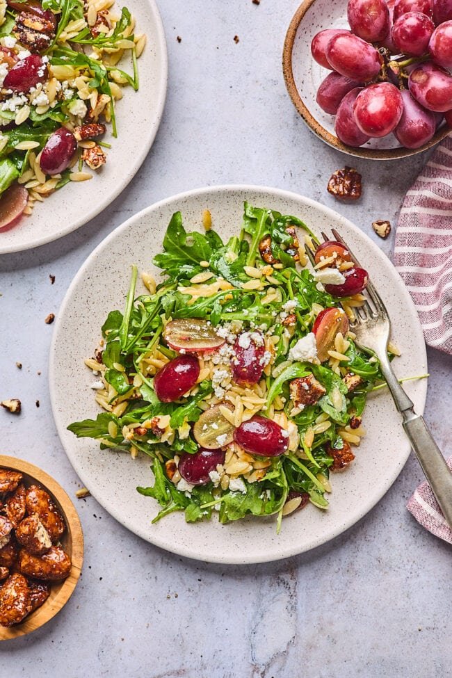 orzo salad with grapes, arugula. feta cheese, candied pecans on plate with fork.
