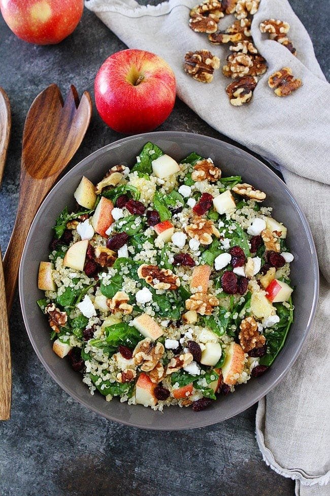 quinoa apple salad with spinach, walnuts, dried cranberries, and goat cheese in bowl. 
