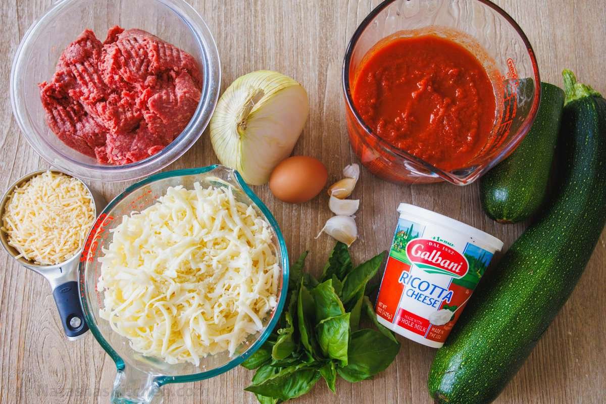 Zucchini lasagna tastes just like the cheesy traditional Italian recipe but with fewer calories and more nutrients. You won't miss the pasta! ingredients for making an Italian layered dish including ground beef, onion, egg, garlic, pasta sauce, mozzarella cheese, basil, ricotta cheese and squash