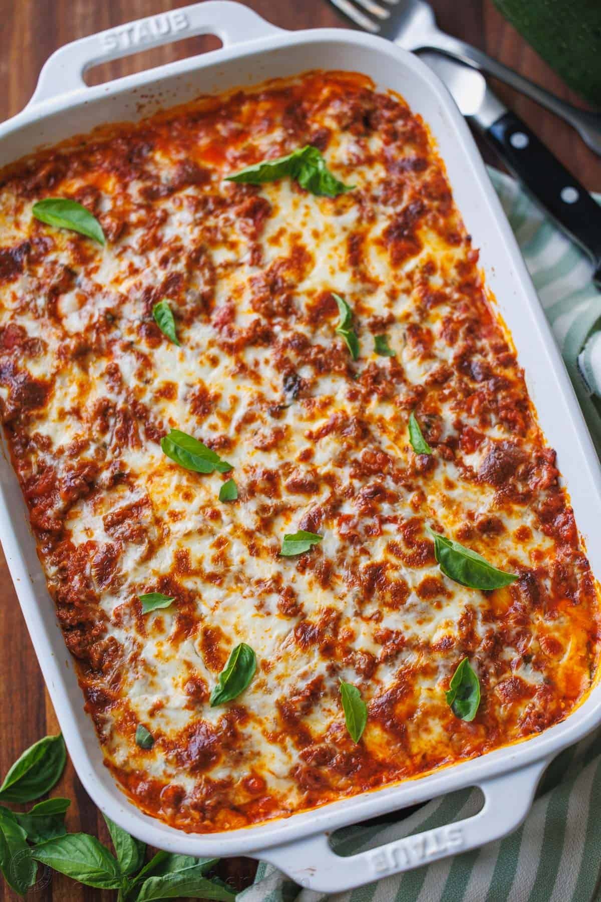 Zucchini lasagna tastes just like the cheesy traditional Italian recipe but with fewer calories and more nutrients. You won't miss the pasta! lasagna with basil in a large white dish