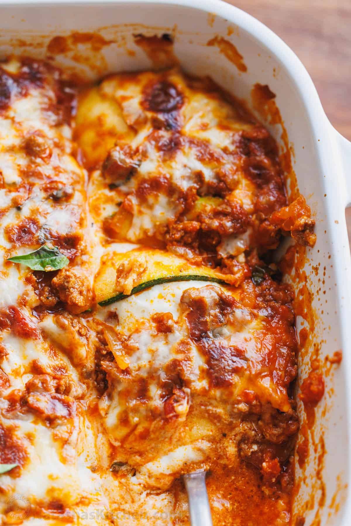 Zucchini lasagna tastes just like the cheesy traditional Italian recipe but with fewer calories and more nutrients. You won't miss the pasta! zoomed in shot of zucchini lasagna with zucchini slice and basil leaf