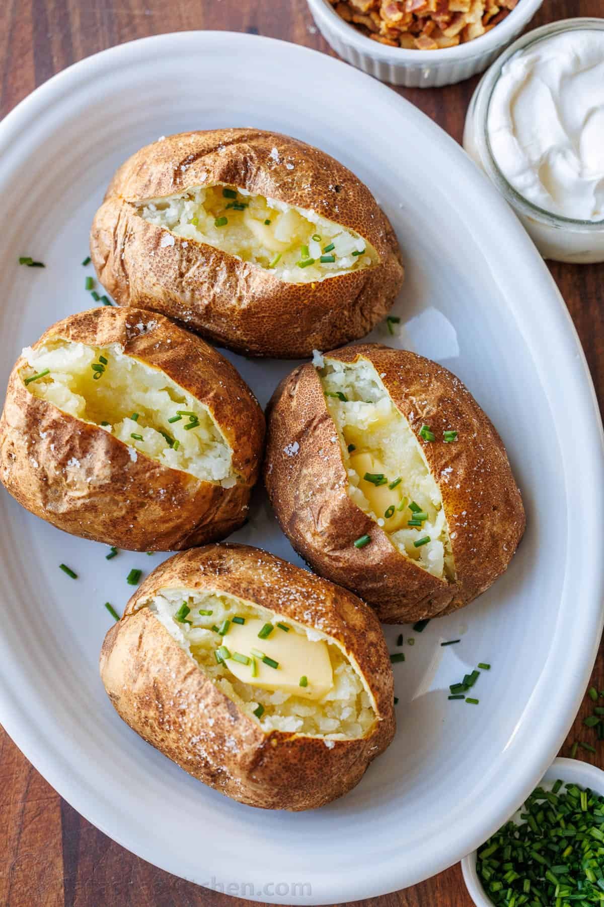 My easy Air Fryer Baked Potato recipe makes the best Baked Potatoes. You'll love the crispy skin with a soft and fluffy center in less time! Air fryer baked potatoes served on white platter with butter and chives