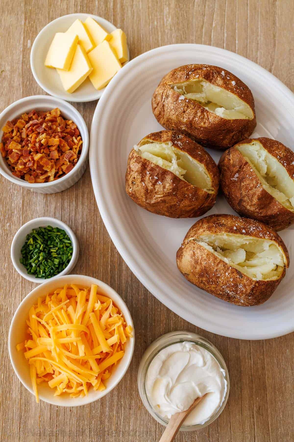 My easy Air Fryer Baked Potato recipe makes the best Baked Potatoes. You'll love the crispy skin with a soft and fluffy center in less time! Baked potato bar with air fryer baked potatoes and toppings in bowls