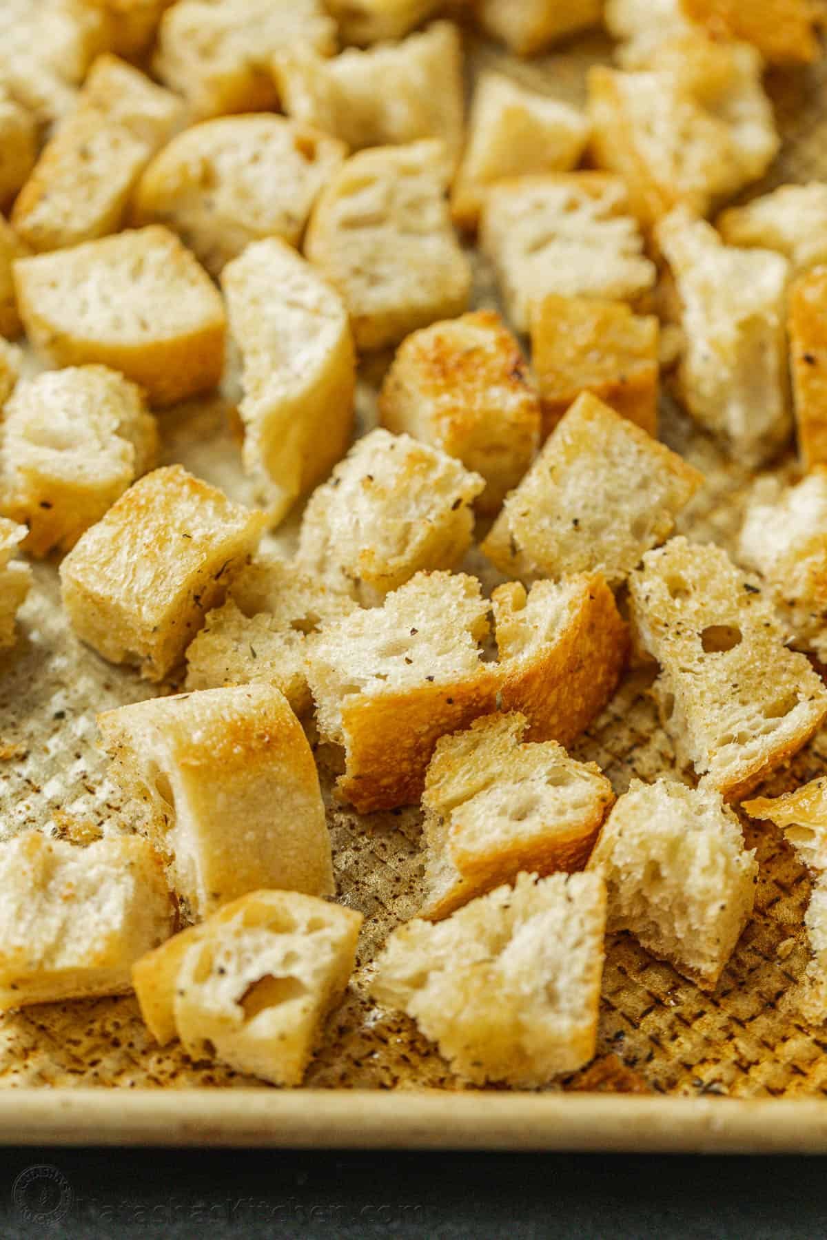 Turn day-old bread into crunchy homemade croutons! Toss these oven-baked garlic croutons over a Caesar salad or snack on them by the handful. Homemade croutons on a metal baking sheet.