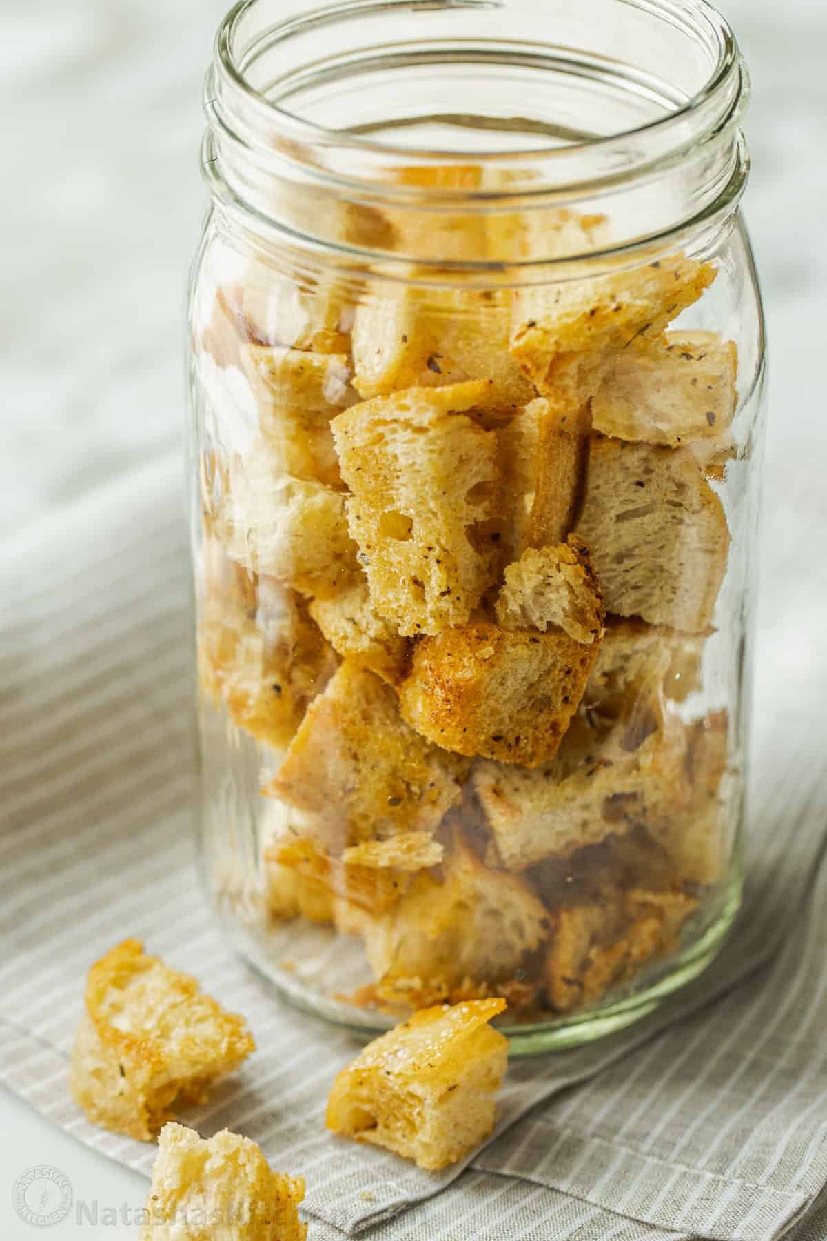 Turn day-old bread into crunchy homemade croutons! Toss these oven-baked garlic croutons over a Caesar salad or snack on them by the handful. Homemade croutons stored in a glass mason jar.