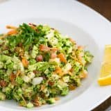 A bowl of loaded broccoli radish salad with a slice on lemon beside it
