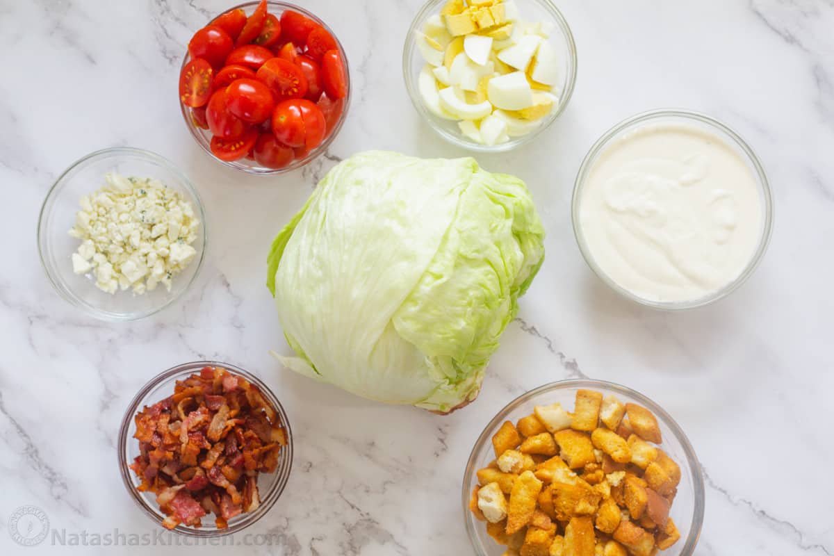 How to make the best Wedge Salad with iceberg lettuce, dressing, bacon, eggs, tomatoes, croutons, a creamy dressing, and blue cheese crumbles Ingredients for wedge salad in ramekins on a platter.