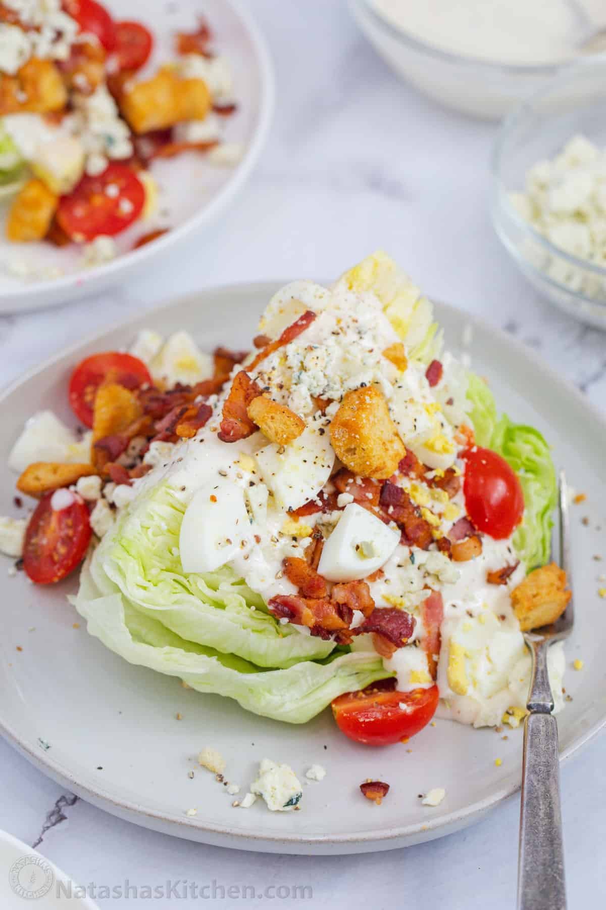 How to make the best Wedge Salad with iceberg lettuce, dressing, bacon, eggs, tomatoes, croutons, a creamy dressing, and blue cheese crumbles Wedge Salad serving suggestion with toppings