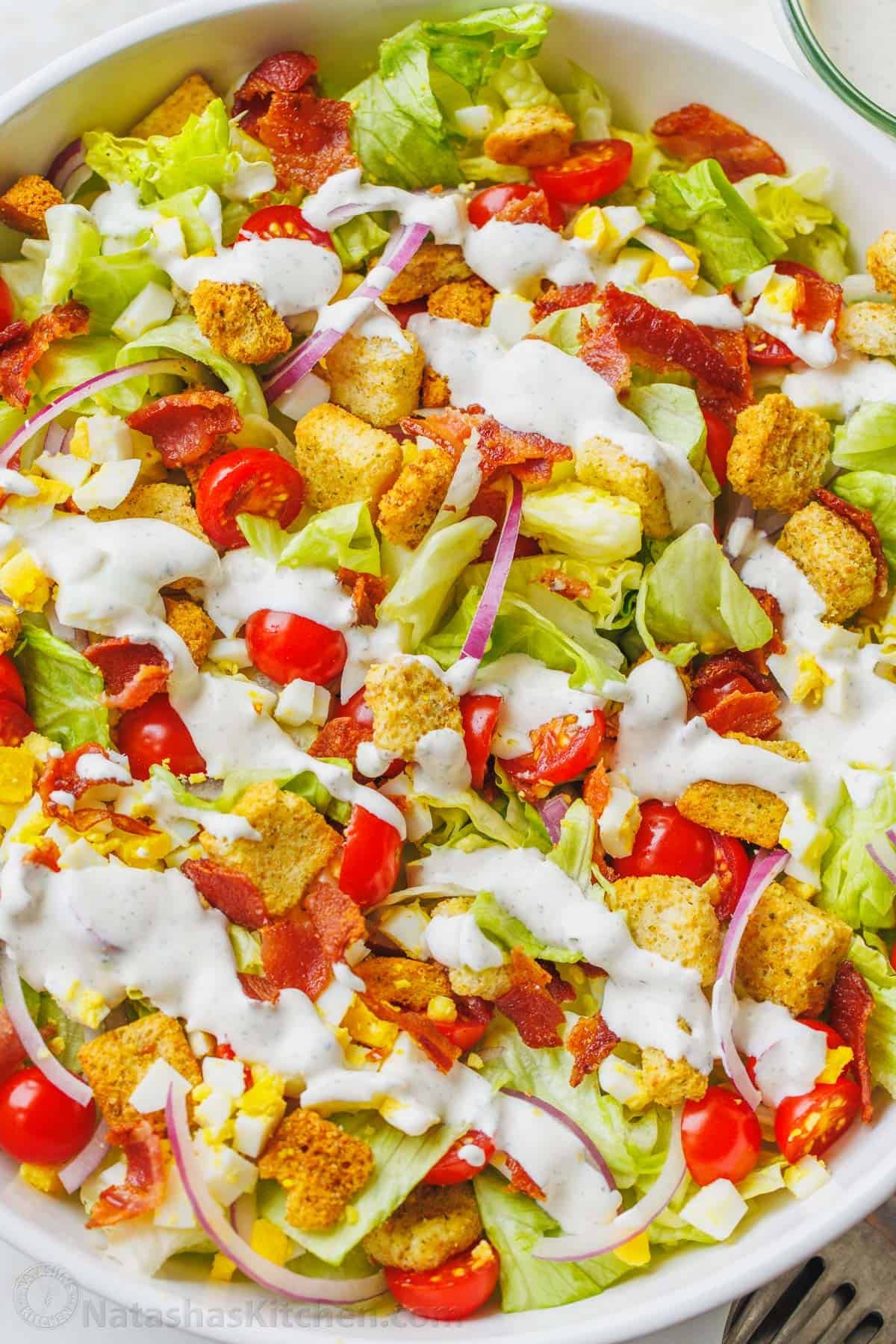 This restaurant-style Garden Salad is an easy salad recipe full of fresh ingredients and tossed with tangy homemade buttermilk dressing. Close up of homemade garden salad in a large white bowl topped with croutons and drizzled with Ranch dressing.