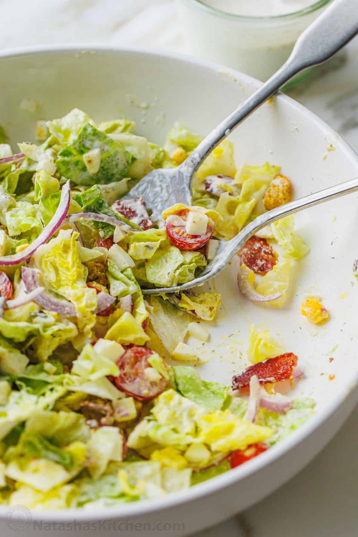 This restaurant-style Garden Salad is an easy salad recipe full of fresh ingredients and tossed with tangy homemade buttermilk dressing. A half-empty bowl of garden salad with two serving spoons.