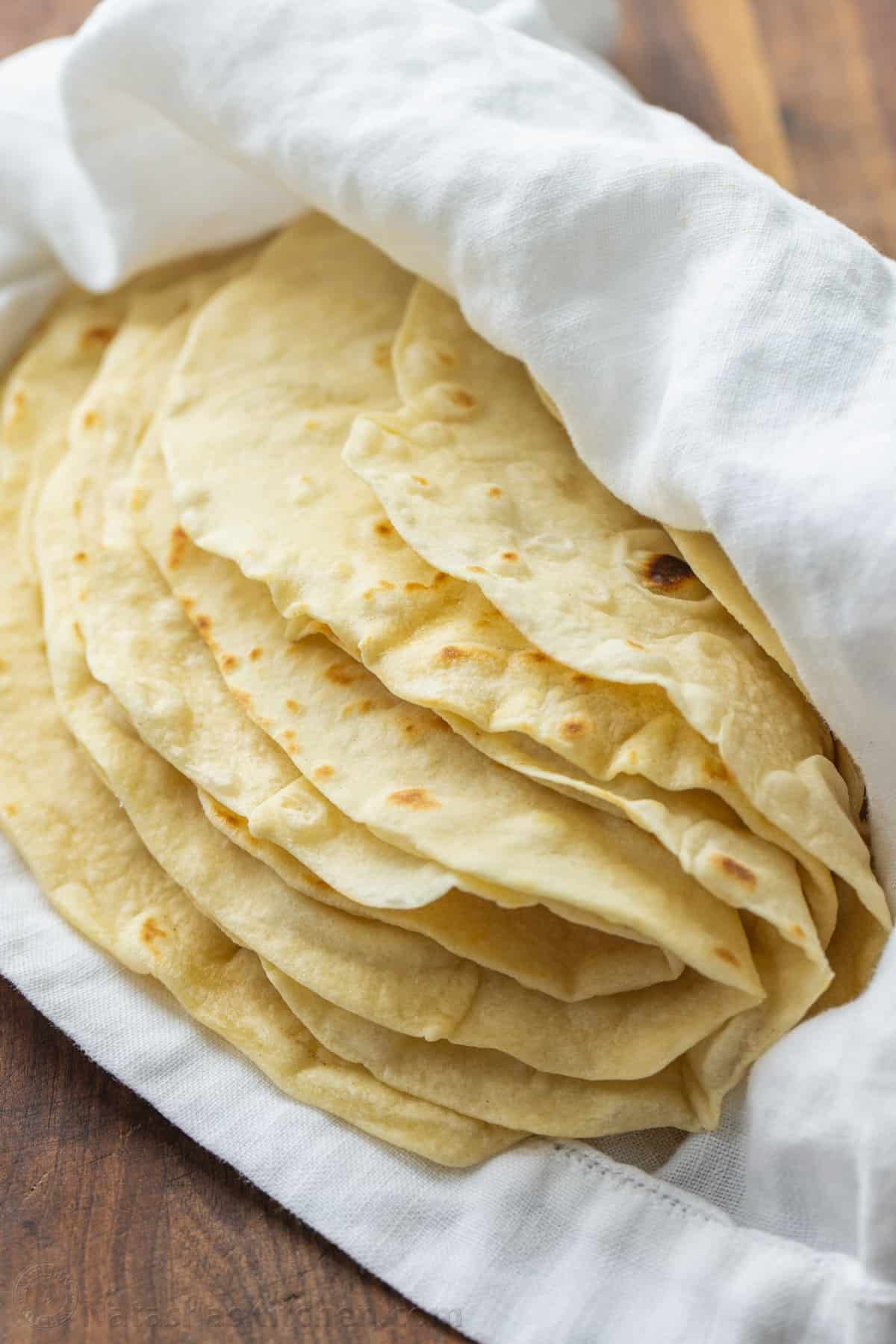 A stack of flour tortillas folded inside a white kitchen towel to keep warm.