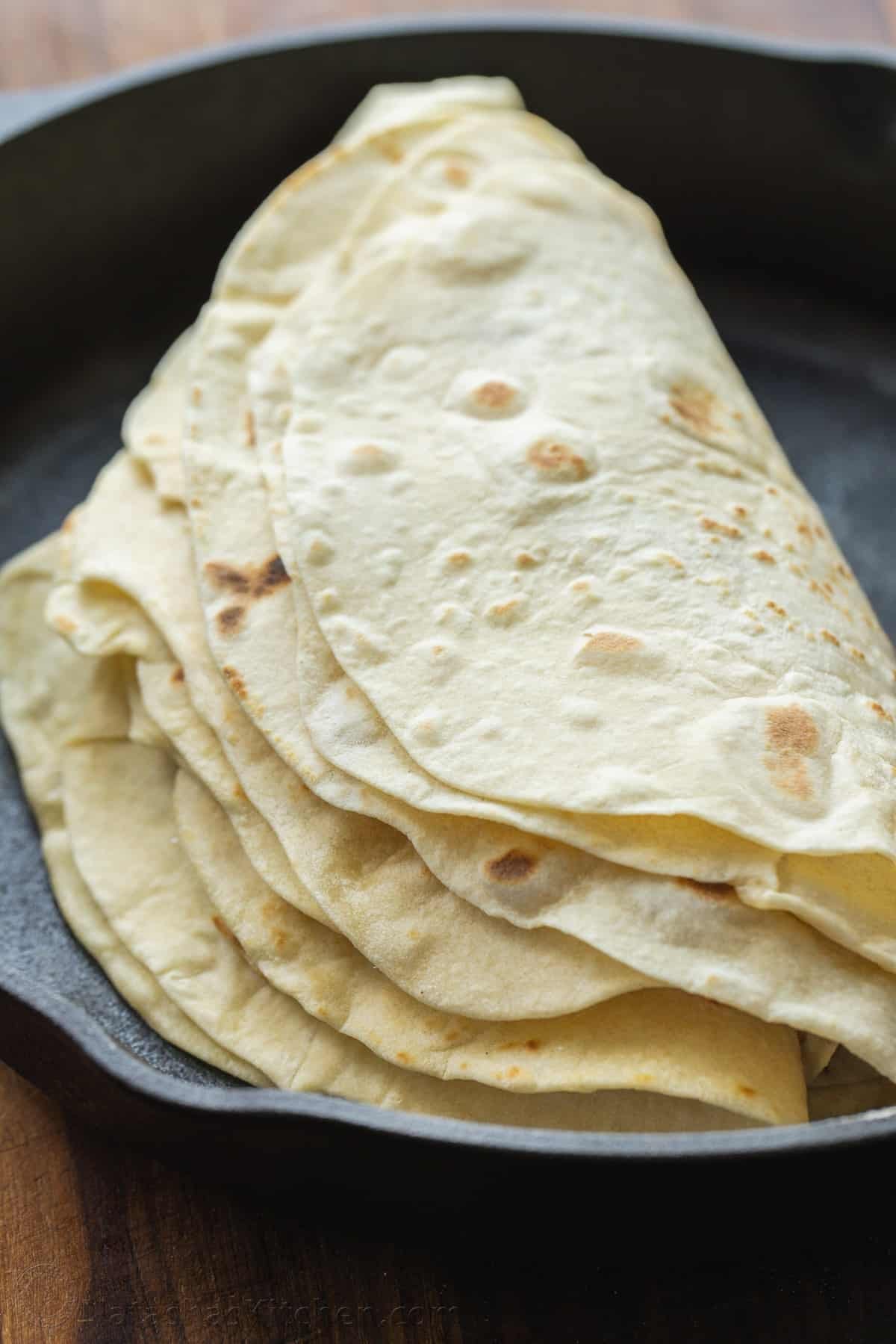 A stack of homemade flour tortillas folded in half inside a skillet.