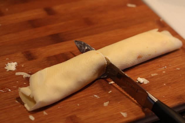 A crepe with filling rolled and cut in half on a cutting board 