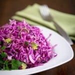 A plate of red cabbage and avocado salad with a fork and cloth napkin beside it