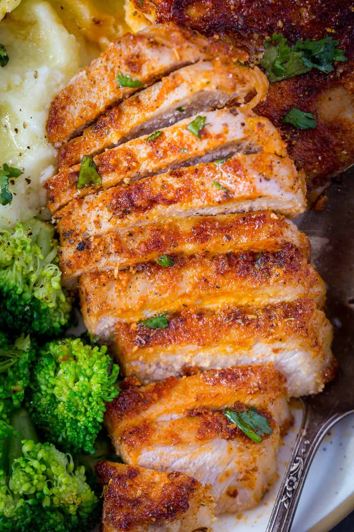 Juicy pork chop cut into slices topped with fresh greens. 