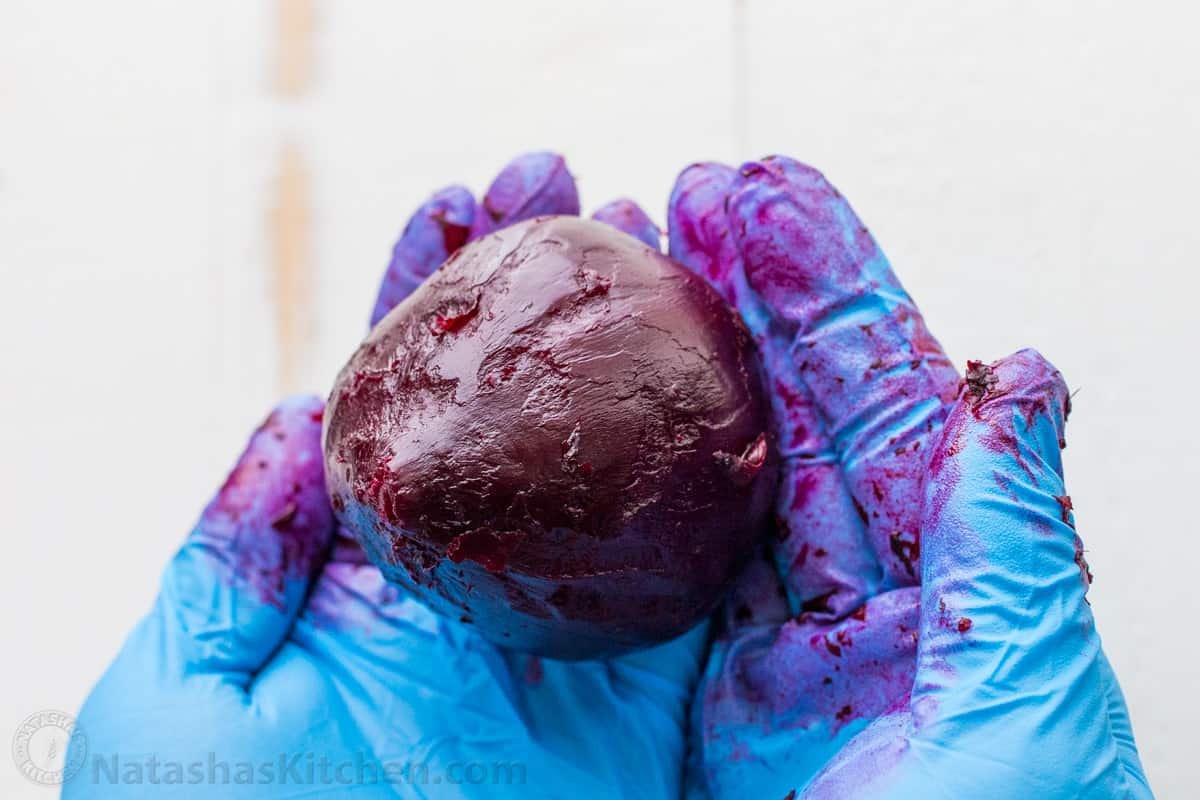 How to peel roasted beets for beet salad A close up of cooked beet being held in hands with gloves on