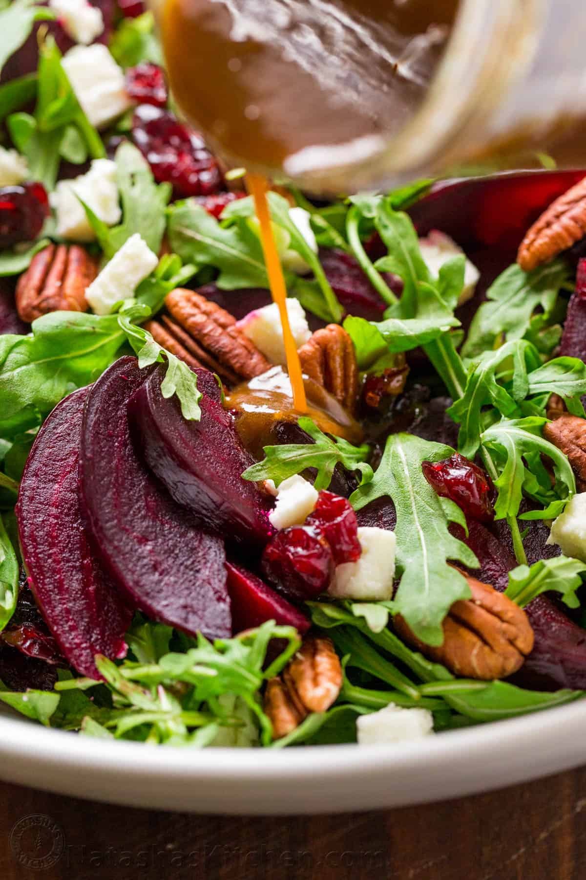 This beet salad recipe tastes fancy but is SO EASY to make. A show-stopping and flavorful salad that is impressive for holidays, entertaining, or dinner at home. Balsamic vinaigrette being poured onto arugula salad with beets