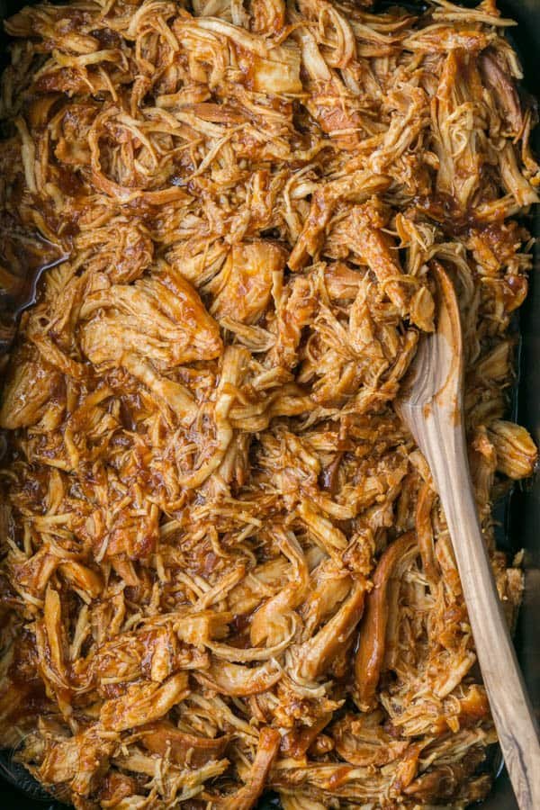 A pile of BBQ chicken with a wooden spoon in the chicken. 