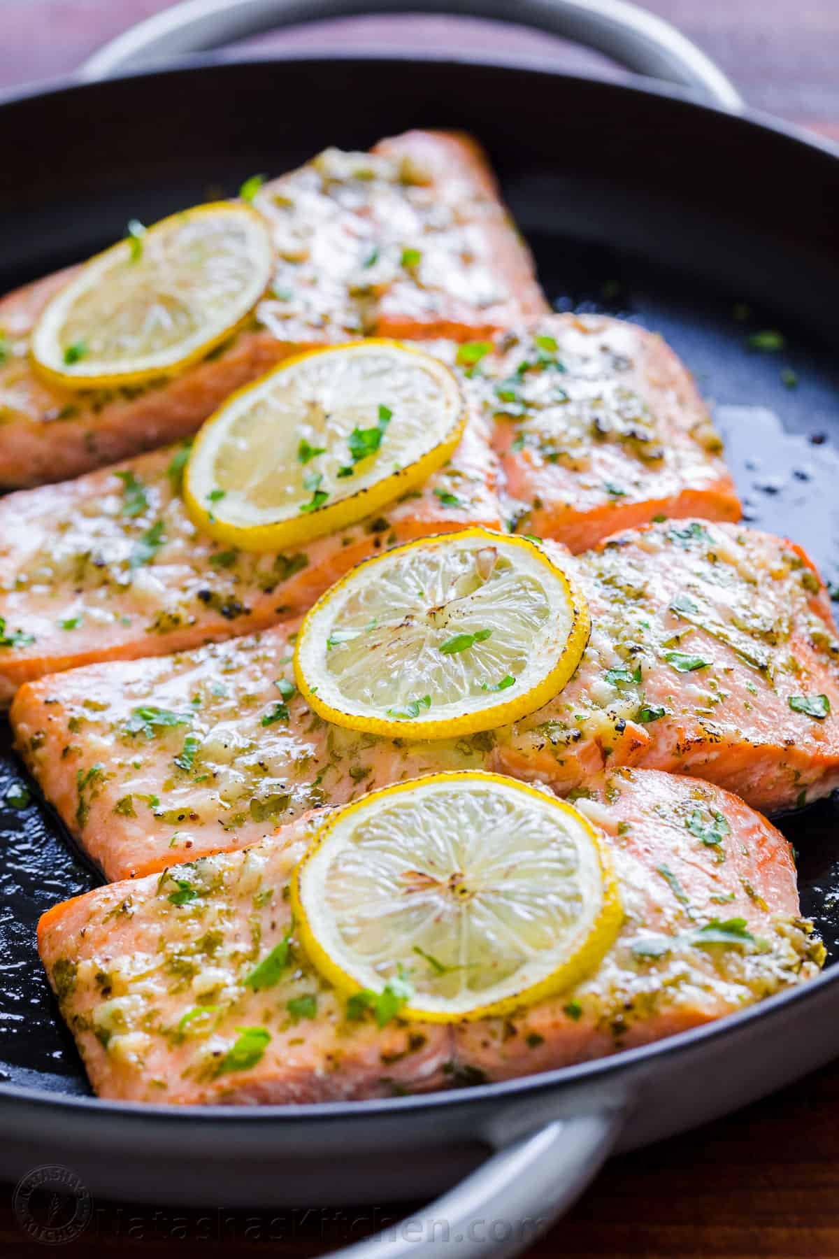 A skillet with four salmon fillets with lemon slices on top. 