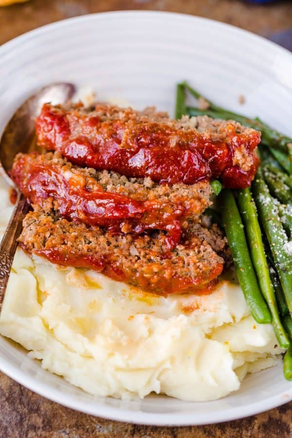 A plate of food, with three meatloaf slices on top of mashed potatoes and asparagus on the side. 