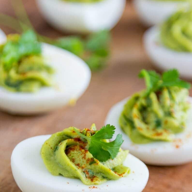 Guacamole Stuffed Eggs on a wooden board garnished with cilantro and paprika