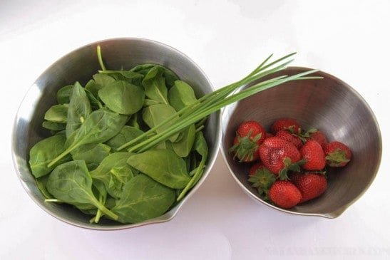 Two bowls one of spinach and green onion and one of strawberries 