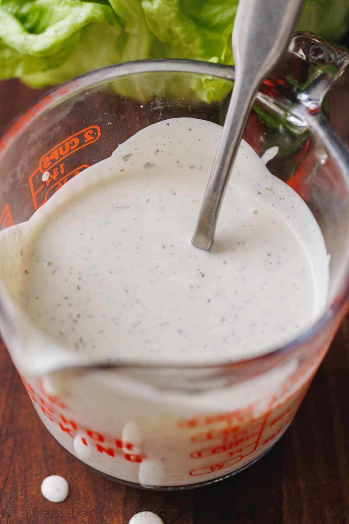Make restaurant-style buttermilk Ranch Dressing in seconds! This creamy homemade ranch recipe is perfect as a salad dressing or as a dip. Buttermilk ranch dressing in a glass measuring cup with a spoon.