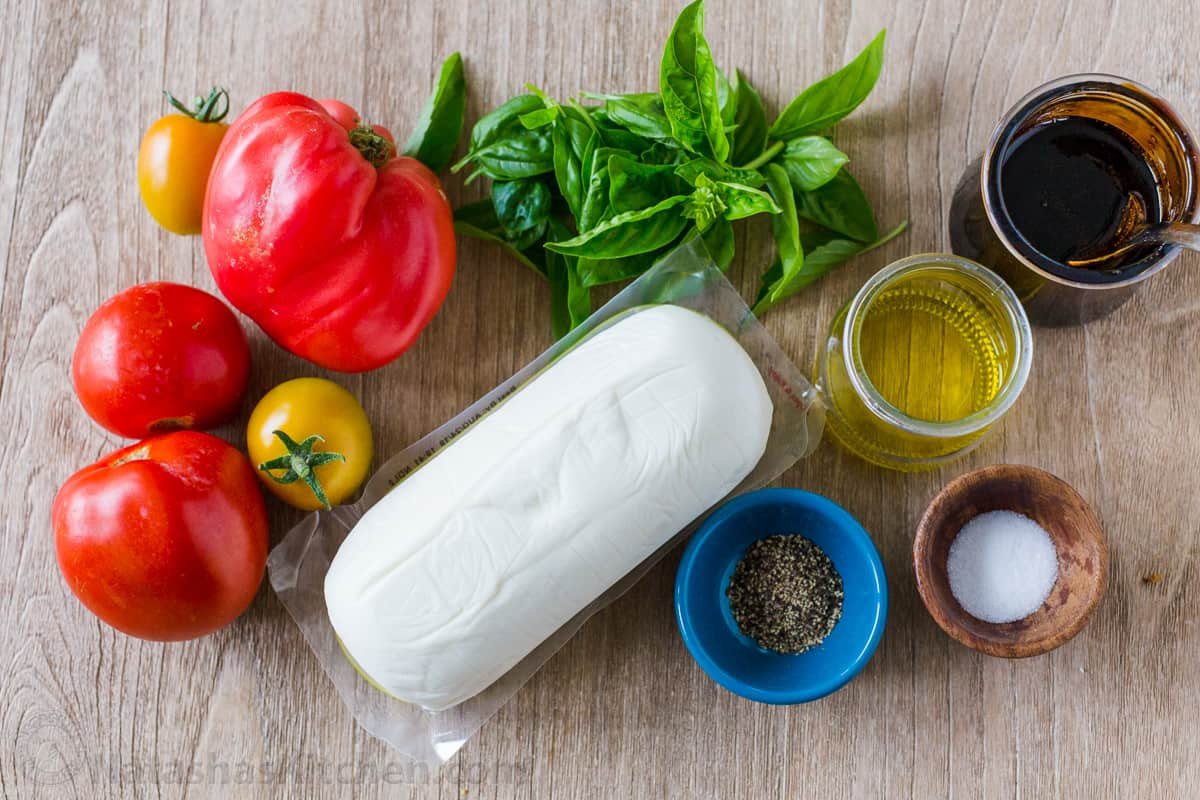 Ingredients to make salad with tomatoes, mozzarella, basil, extra virgin olive oil, salt, pepper, and balsamic glaze