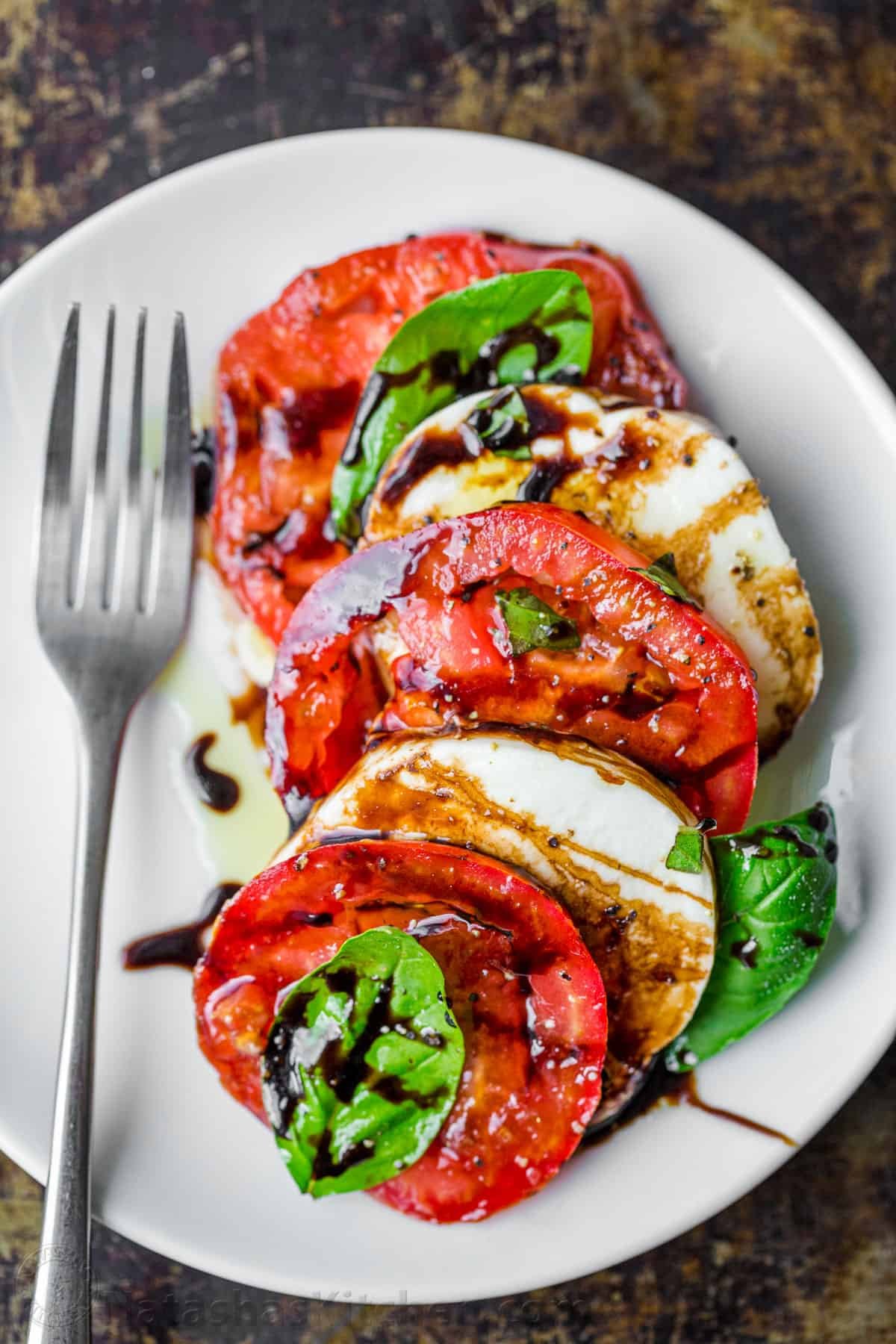 Caprese salad served on a plate with mozzarella, tomatoes, basil and drizzled with balsamic glaze and extra virgin olive oil