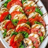 Caprese salad assembled on white platter drizzled with balsamic glaze