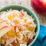 A green bowl of sauerkraut garnished with apples