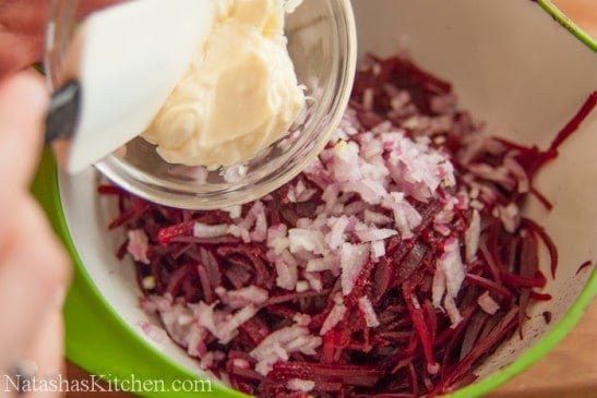 Mayo being added into a large bowl of beets and red onions with a spatula 