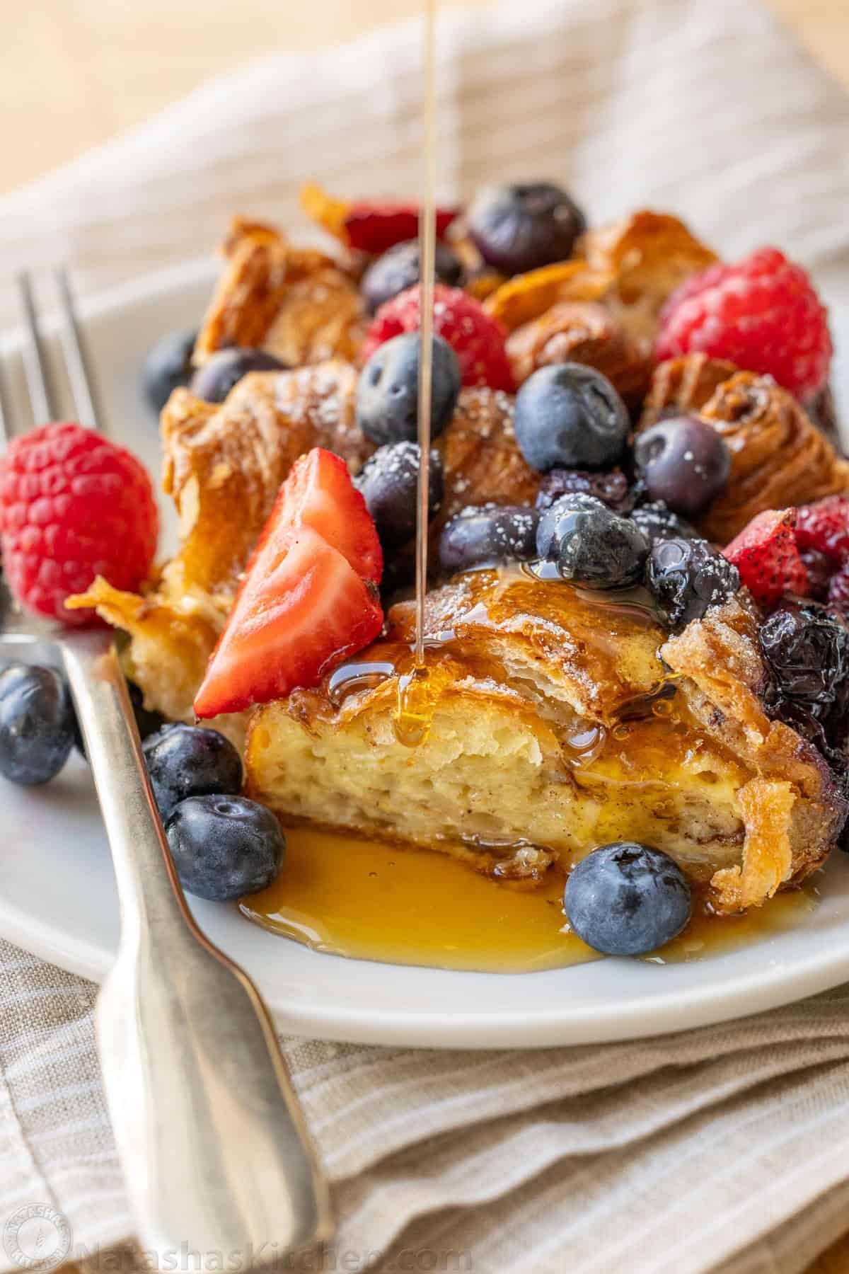 syrup drizzled on Croissant French Toast Bake with fresh berries on top and a fork to eat