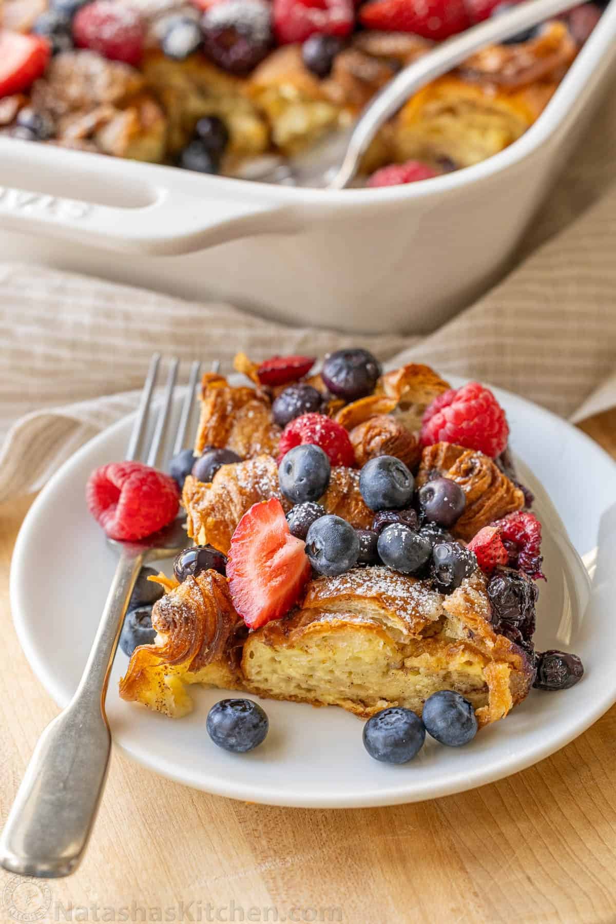Portion of Croissant French Toast Bake on a white plate with berries on top and a fork