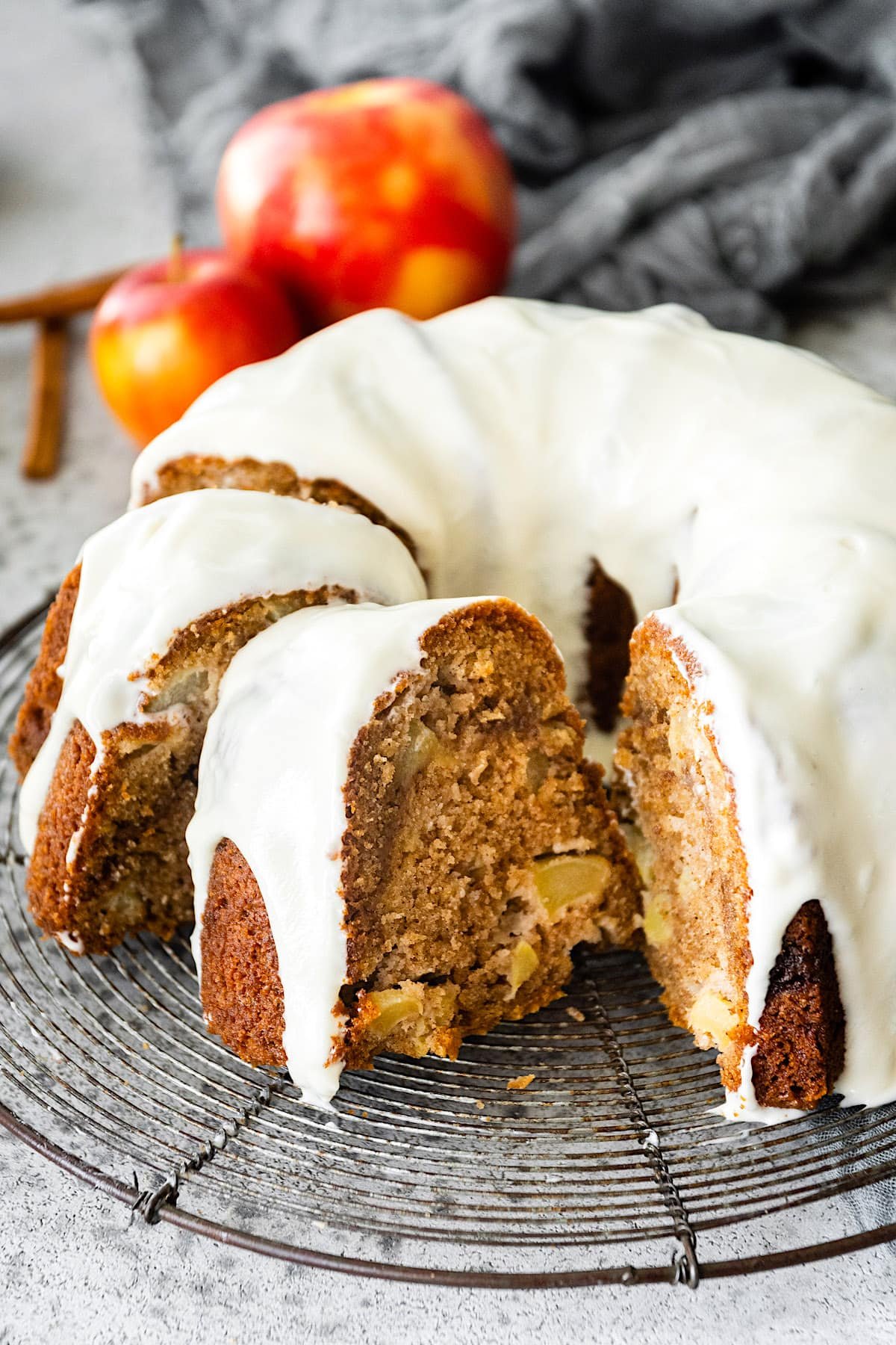 apple bundt cake with cream cheese frosting on cooling rack.