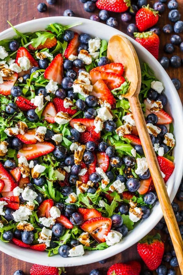 Arugula Salad with berries and goat cheese in bowl drizzled with balsamic glaze