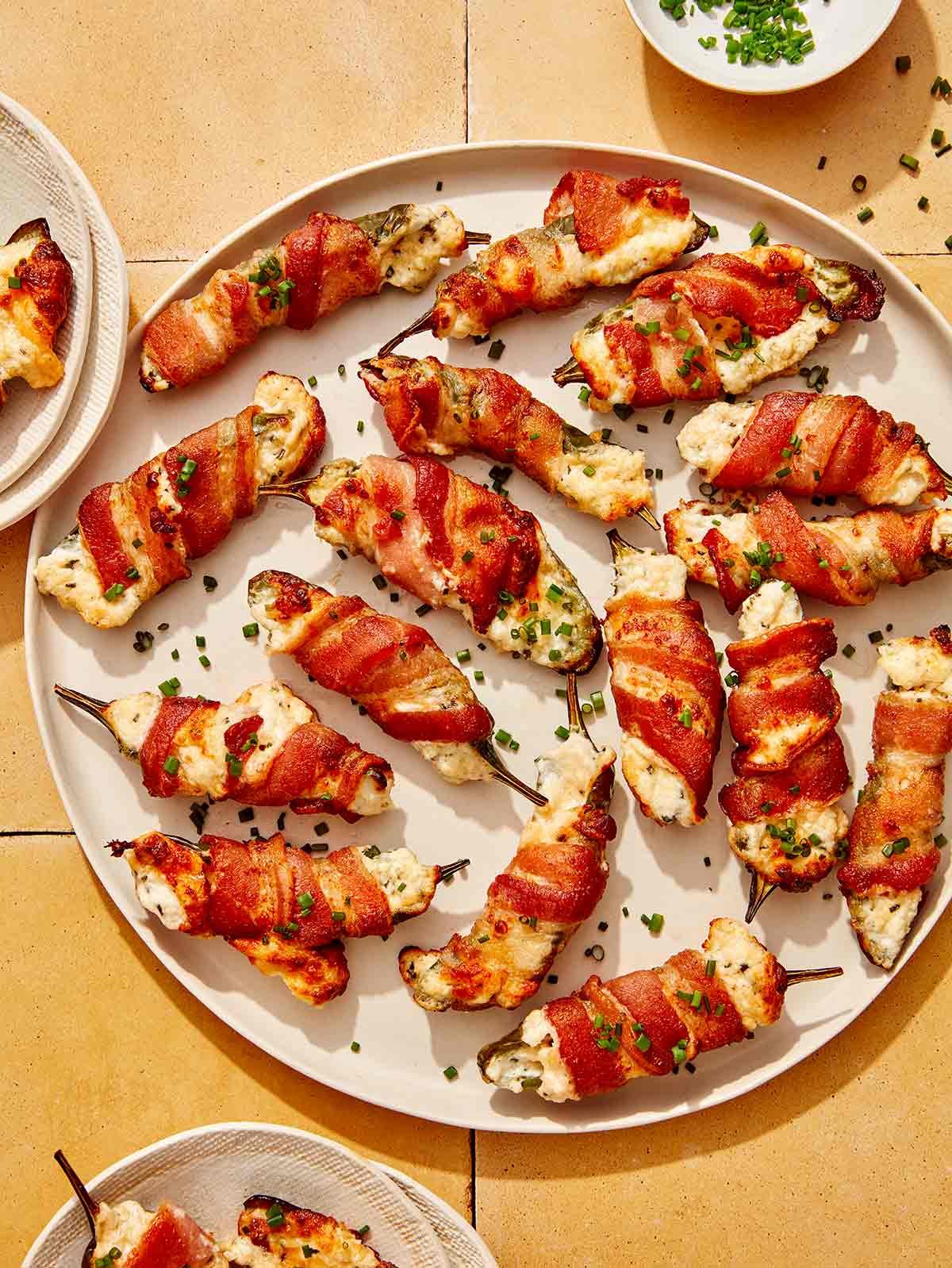 A platter full of jalapeno poppers with some on plates. 