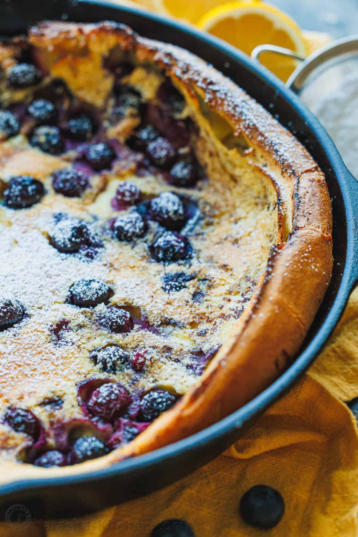 blueberry lemon dutch baby in skillet sprinkled with powdered sugar