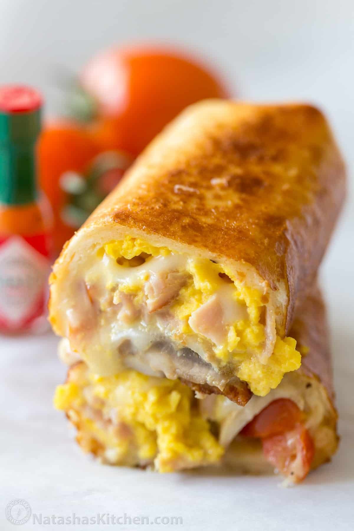 These Breakfast Burritos are easy, fully customizable, and freezer-friendly! Crisp on the outside and filled with egg, ham, and cheese. Stacked Breakfast Burritos sliced in half to showcase egg, ham, and cheese.
