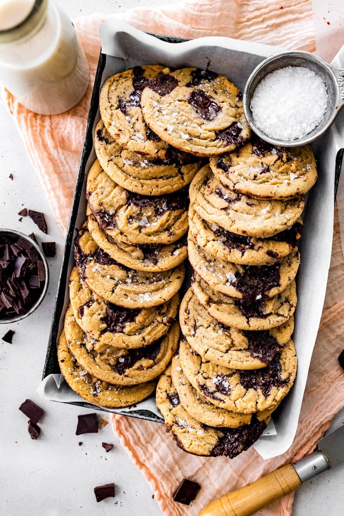 brown butter chocolate chip cookies with flaky sea salt in pan with parchment paper and a bottle of milk.