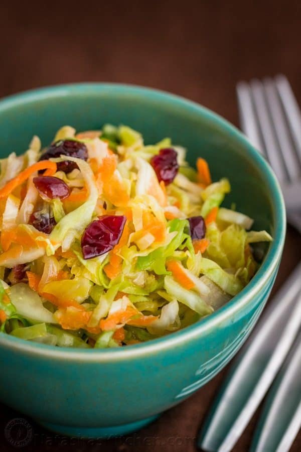 A close up of a green bowl of cabbage, carrot and cranberry salad