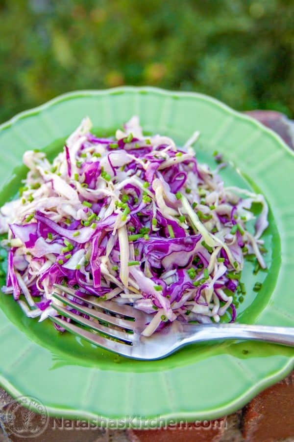 Cabbage and cucumber salad on a green plate with a fork beside it 