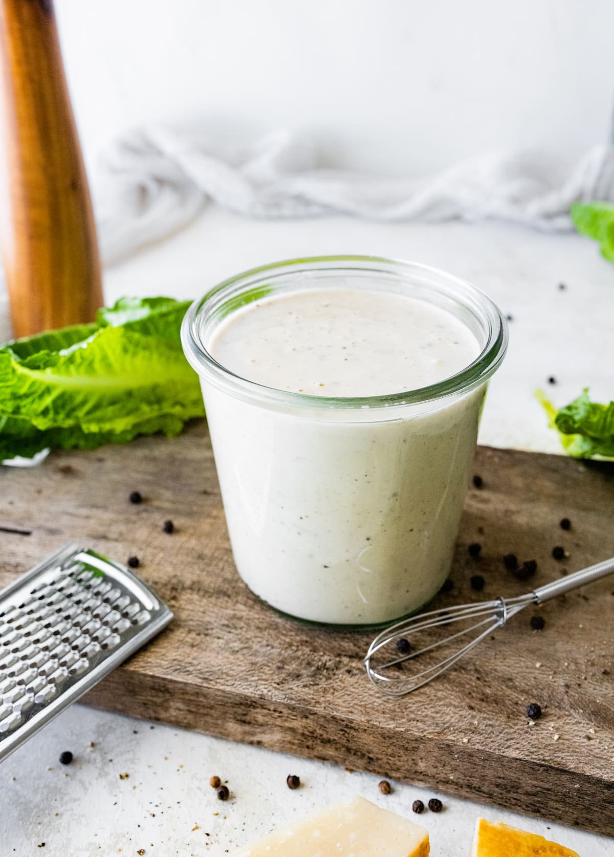 caesar dressing in jar with little whisk on wood cutting board.