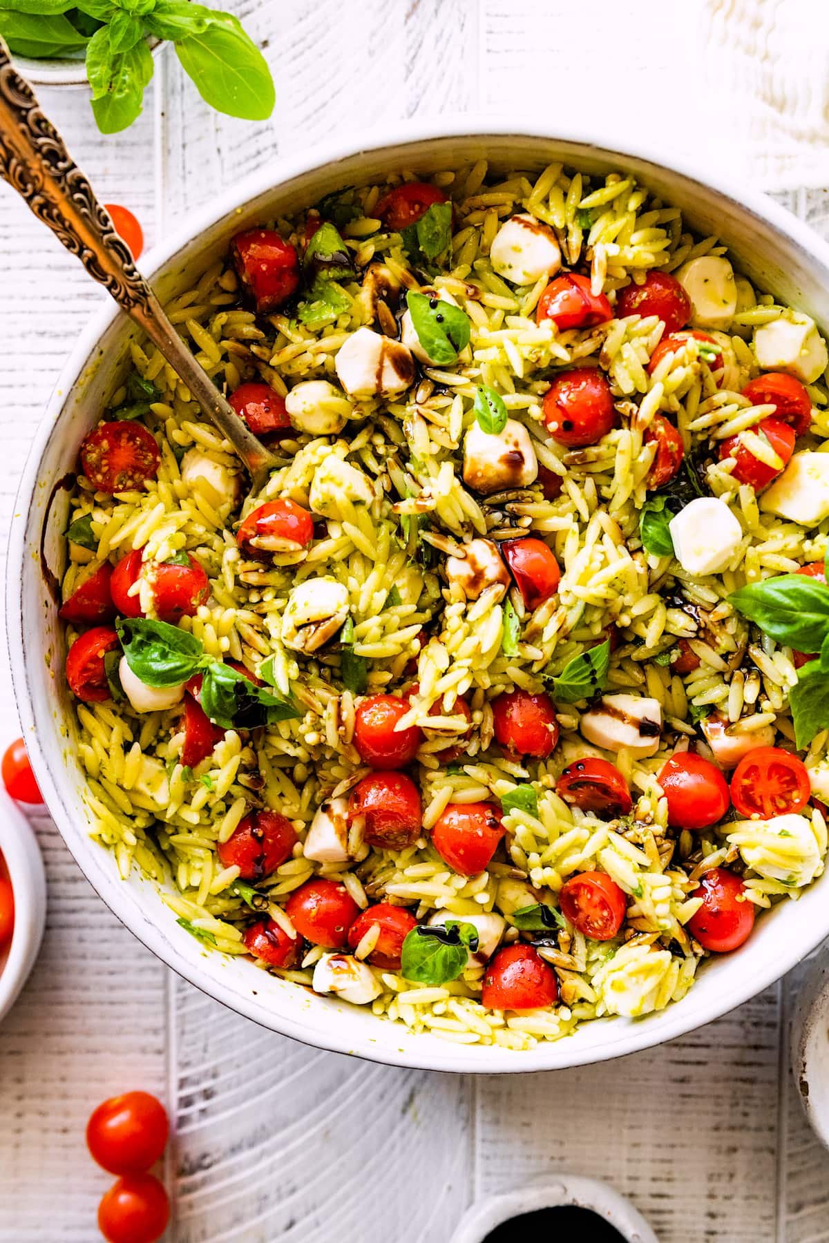 caprese orzo salad with fresh basil, mozzarella, tomatoes, and balsamic in large bowl with spoon.